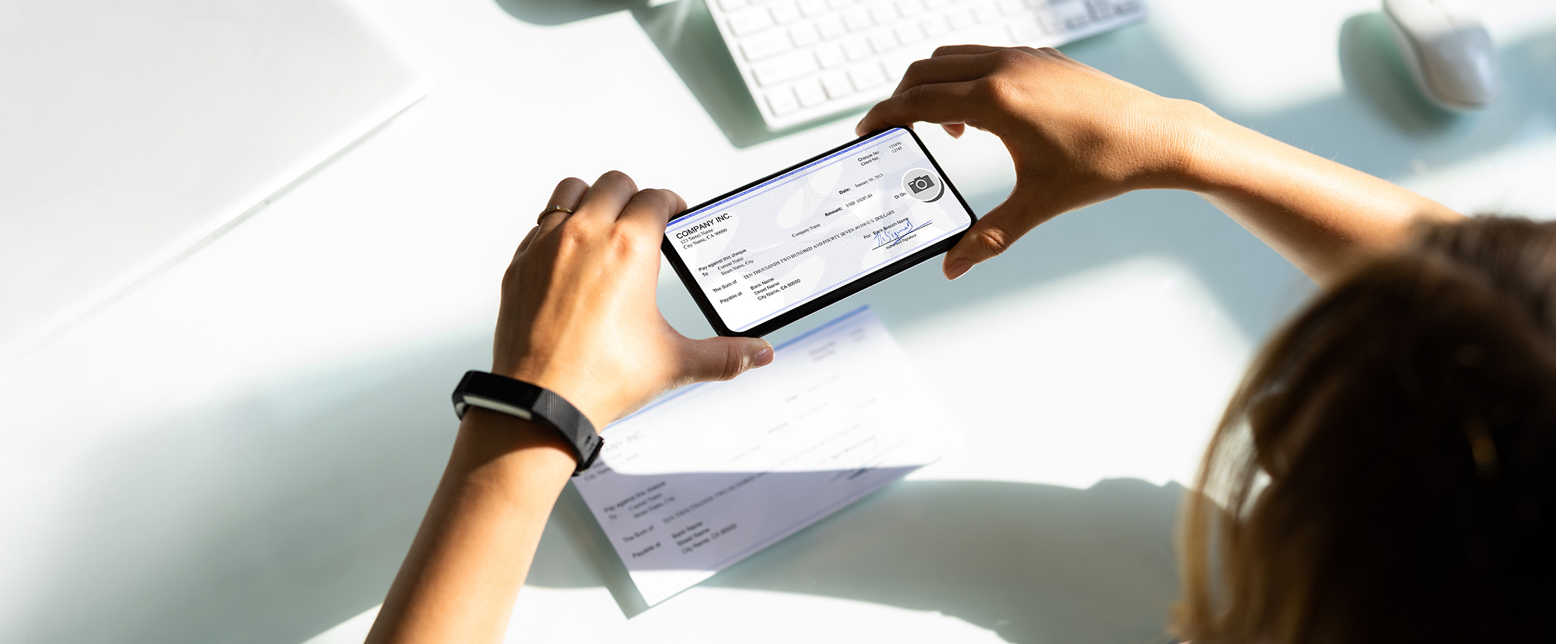 Eine Frau scannt mit ihrem schwarzen Smartphone einen Kontoauszug. Dieser liegt auf einem weißen, aufgeräumten Schreibtisch.