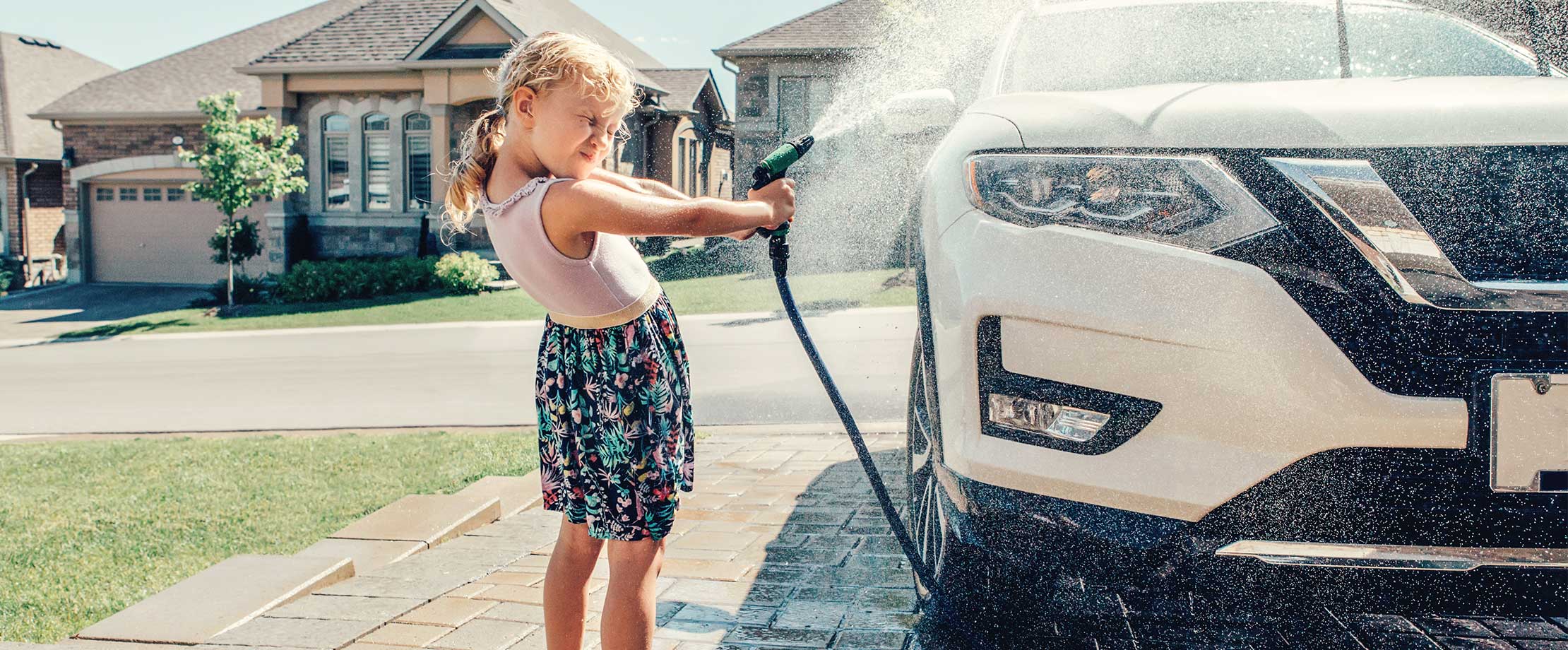 Kleines Mädchen hilft mit dem Gartenschlauch beim Autowaschen